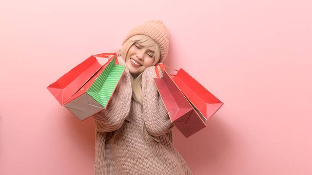 Portrait of Caucasian young woman wearing sweater holding  shopping bag over pink background - Fotoğraf, Görsel