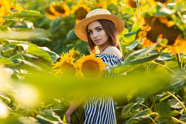 Young woman in hat enjoying summer in sunflower field at sunset. - Φωτογραφία, εικόνα