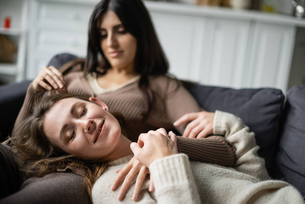 Smiling lesbian woman lying near blurred girlfriend on couch  - Фото, зображення