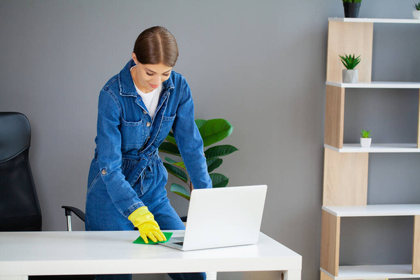Young female worker cleaning office in yellow gloves. - Foto, imagen