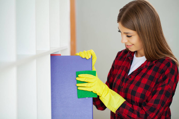 Young girl wiping shelf and folders, office cleaning concept. - Photo, Image
