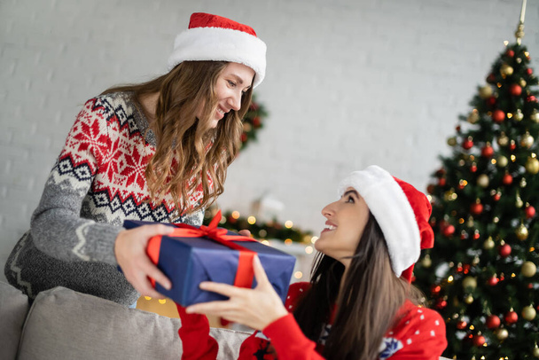 Junge Frau mit Weihnachtsmann beschenkt Freundin bei Silvesterfeier zu Hause  - Foto, Bild
