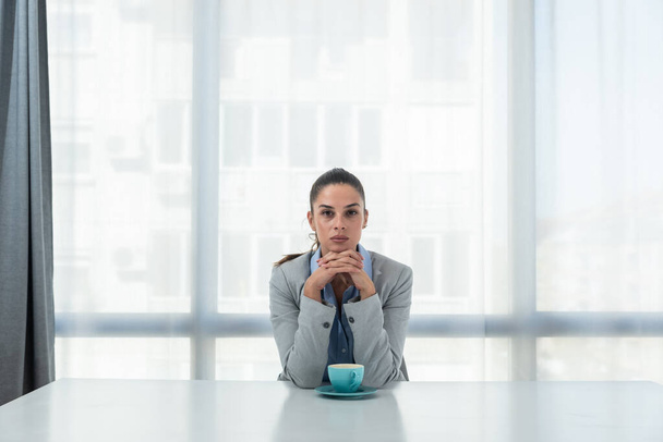 But first coffee. Young tired business woman in formal wear sitting in the office at empty desk with cup of coffee. Female white collar worker, freelancer financial expert morning routine. - Foto, Imagen