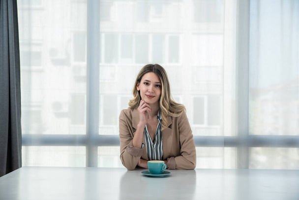But first coffee. Young tired business woman in formal wear sitting in the office at empty desk with cup of coffee. Female white collar worker, freelancer financial expert morning routine. - Foto, Imagen