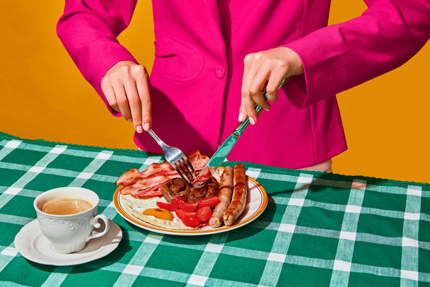 Kobieta jedząca angielskie śniadanie z jajkami, bekonem, kiełbasą, grzybami i pomidorami na zielonym obrusie z kawą. Vintage, styl retro. Sztuka pop-food. Uzupełniające kolory. Kopiuj miejsce na reklamę, tekst - Zdjęcie, obraz