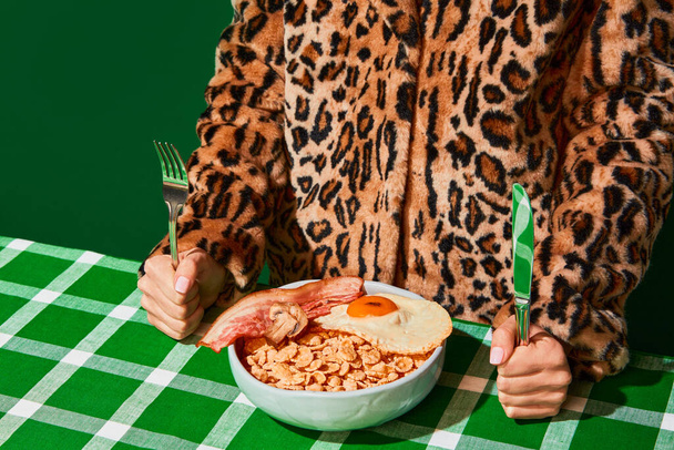 Plate of sweet cornflakes with milk, fried eggs and bacon on green tablecloth. Unordinary combination. Vintage, retro style. Food pop art photography. Complementary colors. Copy space for ad, text - Foto, Bild