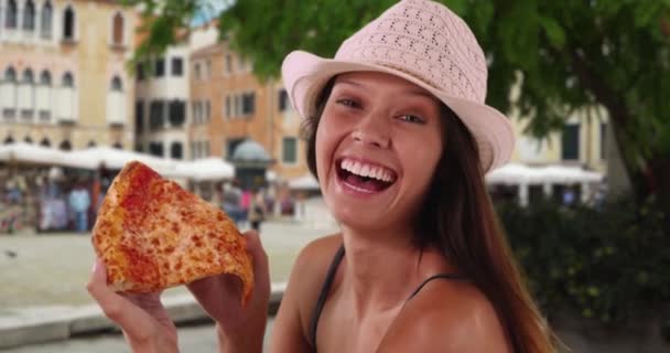 Young tourist woman in trendy fedora enjoying vacation in Italy eating pizza. Close up of cheerful female on Venice street exploring Italian cuisine. 4k - Footage, Video