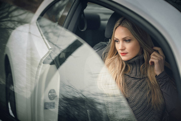 Une œuvre d'art. Une photo d'une belle fille élégante assise dans une voiture. Il y a de belles reflets sur les fenêtres de la voiture. - Photo, image