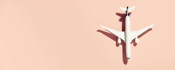 Miniature white airplane on a pink background. Banner, flat lay, creative concept of air transportation, tourism, travel. Copy space for text - Foto, imagen