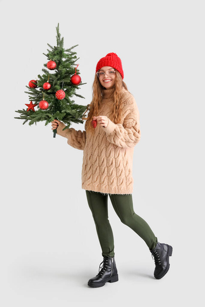 Young woman with Christmas tree and decor on grey background - Photo, Image