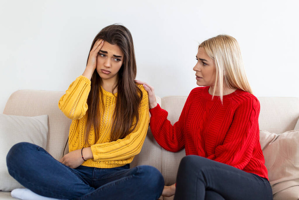 Friend trying to calm down her friend. Woman crying. Young lady sharing her problem with friend. female in depression. Woman comforting hes sad friend sitting on a couch in the living room at home - Photo, Image