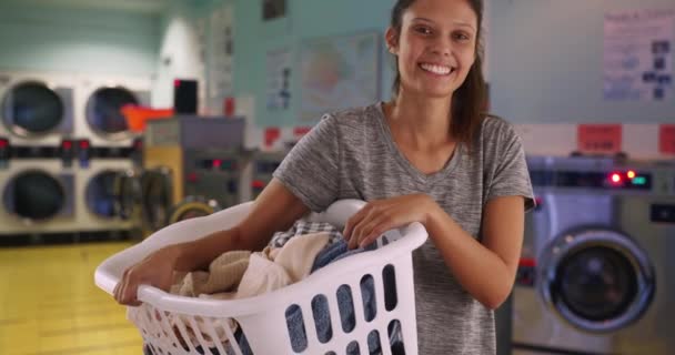 Casual brunette vrouw houden mand van schone kleren in de wasruimte. Jonge blanke vrouw die kleren wast op wasdag. 4k - Video