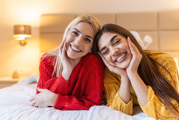 Happy friends lying on bed at home or hotel bedroom smiling posing looking at camera, lazy weekend leisure activities concept - Photo, image