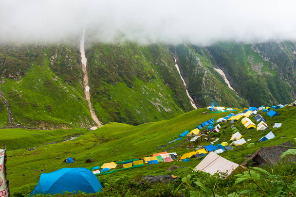 14 juli 2022, Himachal Pradesh India. Meerdere kleurrijke tenten bij basiskamp Bheem Dwari met prachtige bergtoppen en watervallen op de achtergrond. Shrikhand Mahadev Kailash Himalaya Yatra. - Foto, afbeelding