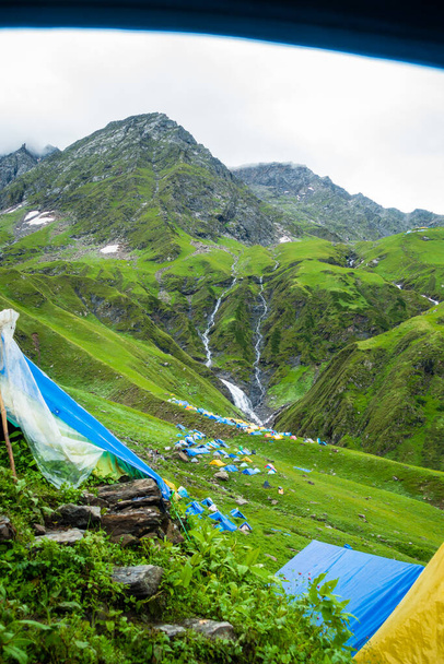 14 juli 2022, Himachal Pradesh India. Meerdere kleurrijke tenten bij basiskamp Bheem Dwari met prachtige bergtoppen en watervallen op de achtergrond. Shrikhand Mahadev Kailash Himalaya Yatra. - Foto, afbeelding
