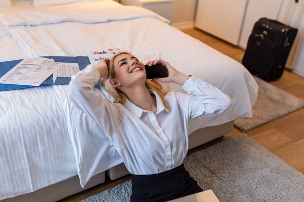 Business Woman working from a hotel room. Beautiful young woman talking on mobile smart phone. Sitting on the ground having fun on business trip - Fotografie, Obrázek