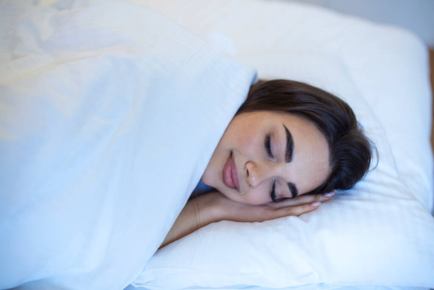 Healthy long dream, comfortable bed with white linen and orthopedic mattress. Young caucasian woman sleeping in the bed, relaxed calm dreams - Photo, Image
