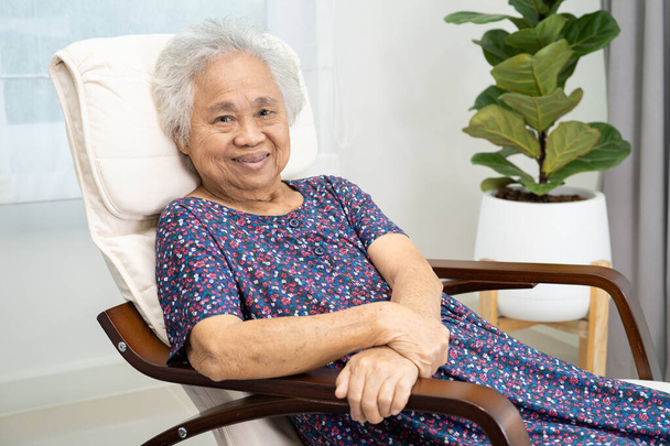 Ázsiai idős nő ül és pihentető boldog hintaszékben a szobában otthon. - Fotó, kép