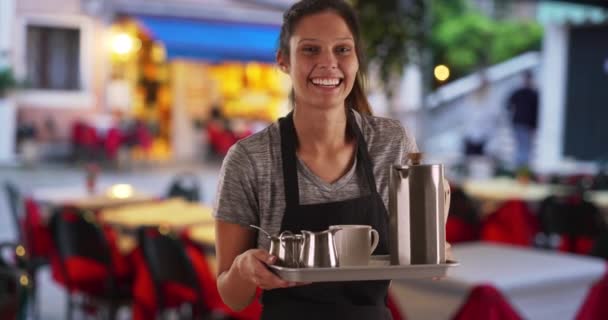 Ładna kelnerka w restauracji, niosąca tacę z kawą i napojami. Piękny przyjazny serwer w fartuchu i tacy do serwowania napojów w kawiarni. 4k - Materiał filmowy, wideo