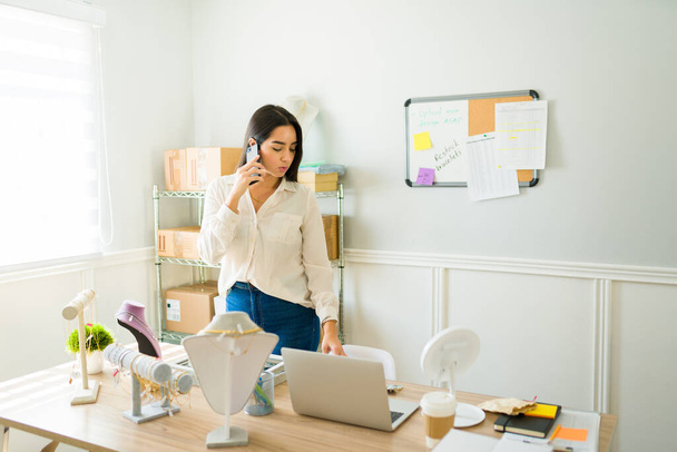 Занятая женщина-предприниматель разговаривает с клиентом по телефону при продаже ювелирных изделий в интернет-магазине - Фото, изображение
