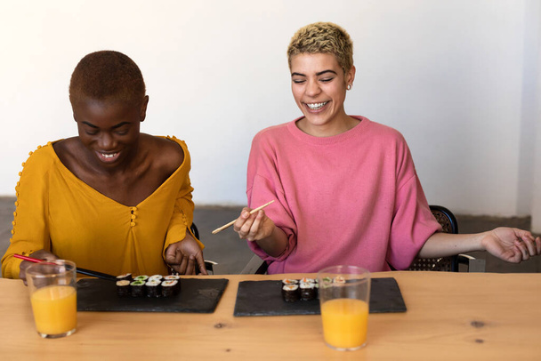 Happy beautiful women sitting while eating vegan sushi rolls - Foto, imagen