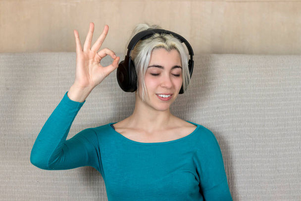 Een vrouw gesloten oog en genieten van de muziek en ontspannen zitten thuis, waardoor OK gebaar - Foto, afbeelding