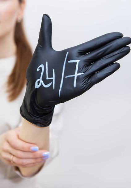 Рука жінки в чорній гумовій рукавичці, на якій написано 24 7, допомога в будь-який час, завжди на зв'язку. Підтримка та концепція допомоги
 - Фото, зображення
