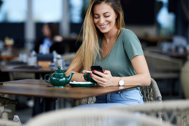 Kobieta siedzi w kawiarni, pije herbatę i używa telefonu do czatu online. - Zdjęcie, obraz