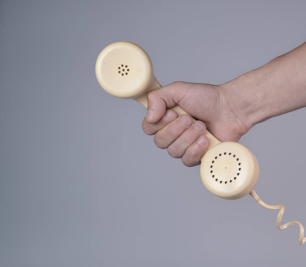 Male hand holding an old plastic telephone receiver on gray background. Close up remote handset from a retro rotary home phone in the hands of man. Concept of communication, conversation, connection - Φωτογραφία, εικόνα