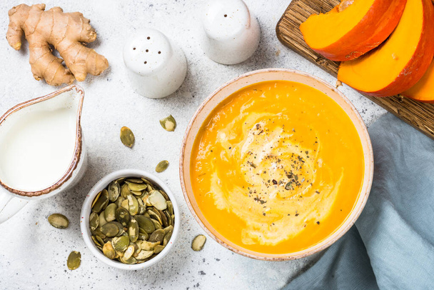 Pumpkin soup puree with cream and seeds in the bowl. Top view image at white table. - Фото, зображення