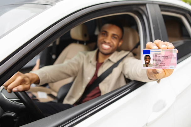 Szczęśliwy młody Afrykanin pokazujący prawo jazdy z otwartego okna samochodu. Wysokiej jakości zdjęcie - Zdjęcie, obraz