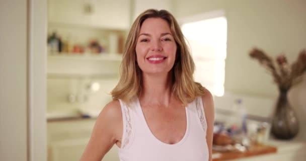 Atrakcyjna biała kobieta w średnim wieku uśmiecha się i całuje przed kamerą w kuchni. Portret flirciarki uśmiechniętej i śmiejącej się z kamery w domu. 4k - Materiał filmowy, wideo
