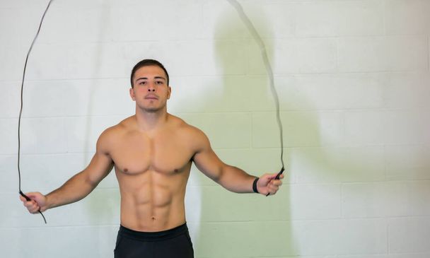 Amazing photo of a handsome muscular young man training by jumping rope. He focuses on performing the exercise, motivational. Copy space. - Foto, Imagen