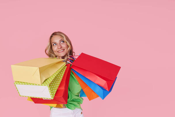 Portrait of an excited joyful young woman with colorful shopping bags on a pink background. Surprised Girl with wide open mouth - Фото, изображение