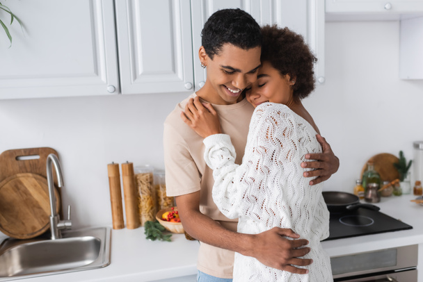 cheerful african american couple hugging near worktop in kitchen - Photo, image
