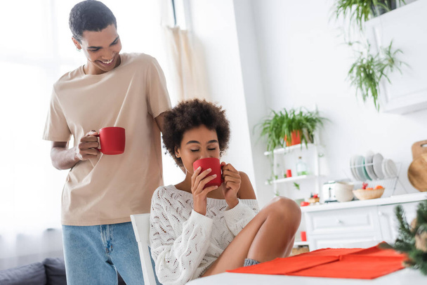 young african american man smiling near sexy girlfriend drinking morning coffee with closed eyes - Foto, Imagem
