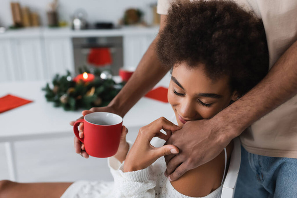 african american man with red cup touching sensual girlfriend in kitchen - Photo, Image