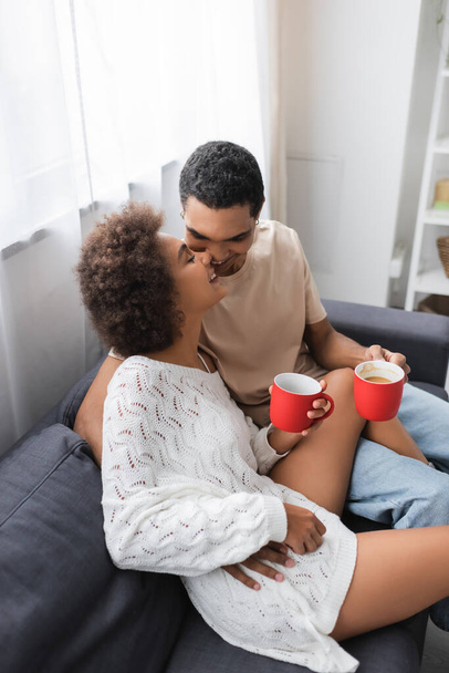 vista de ángulo alto de la pareja afroamericana con copas rojas sonriendo en el sofá en casa - Foto, imagen
