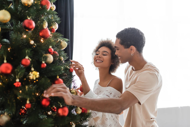 νεαρό και σέξι αφροαμερικάνικο ζευγάρι που στολίζει χριστουγεννιάτικο δέντρο στο σπίτι - Φωτογραφία, εικόνα