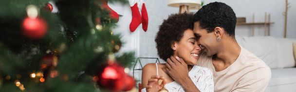 young and happy african american couple embracing near blurred christmas tree, banner - Foto, immagini