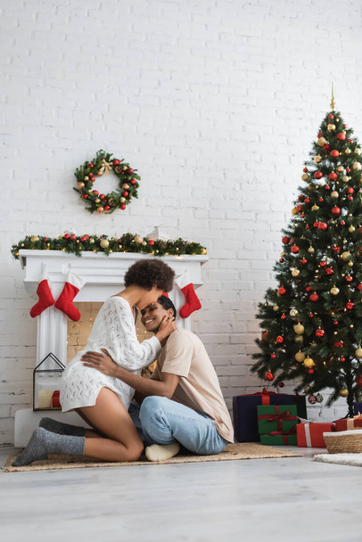 young african american couple embracing near christmas tree and decorated fireplace in living room - Valokuva, kuva