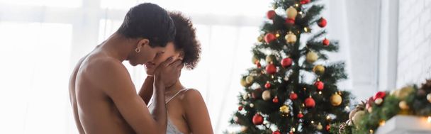 恥知らずなアフリカ系アメリカ人男性キスセクシーな若い女性近くクリスマスツリー,バナー - 写真・画像