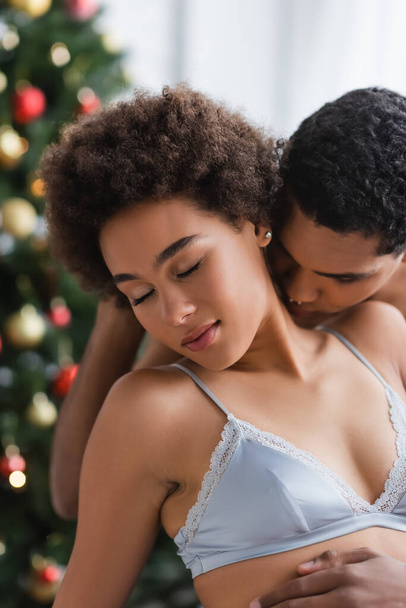young and sexy african american woman with closed eyes near boyfriend kissing her on blurred background - Photo, Image