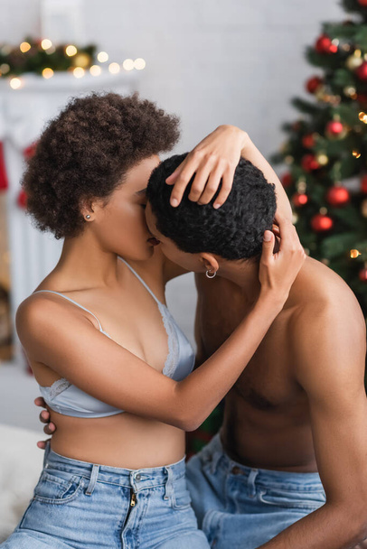 若いと情熱的なアフリカ系アメリカ人のカップルでジーンズ接吻近くぼやけたクリスマスの装飾 - 写真・画像
