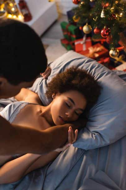 目を閉じたアフリカ系アメリカ人女性の高い角度ビュークリスマス前夜にぼやけたボーイフレンドと愛を作る - 写真・画像