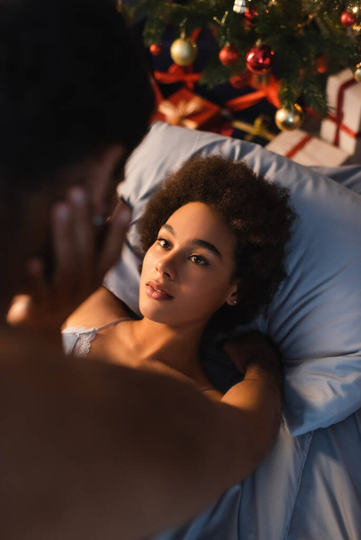 high angle view of curly african american woman lying on bed and touching blurred boyfriend - Photo, Image