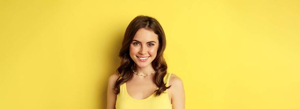 Close up portrait of brunette woman with healthy white smile, looking happy and confident, posing against yellow background. - Foto, Imagen