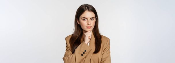 Image of businesswoman thinking, corporate woman looking thoughtful, making decision, standing in brown suit over white background. - Zdjęcie, obraz