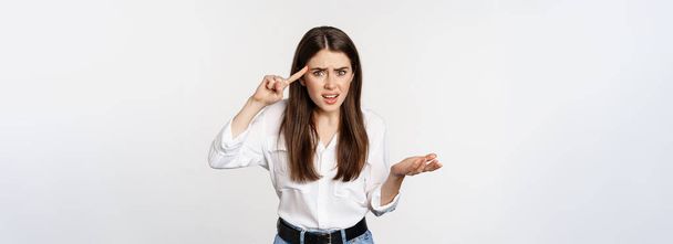 Are you dumb. Annoyed woman scolding, roll finger over head and staring at camera, bothered by someone crazy, standing over white background. - Photo, Image