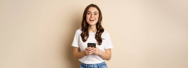 Happy modern woman smiling, holding smartphone and laughing, concept of cellular technology and mobile phone. - Фото, изображение